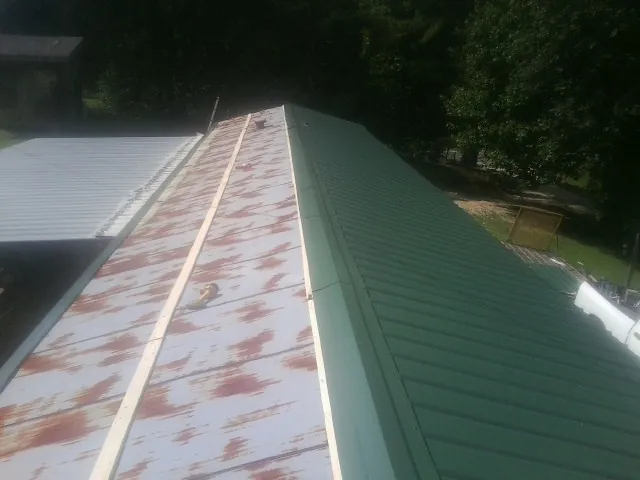 Old rusted panels beside newly installed green metal roofing — Wind Damage Roof Repair by Roofing Brothers in Talent