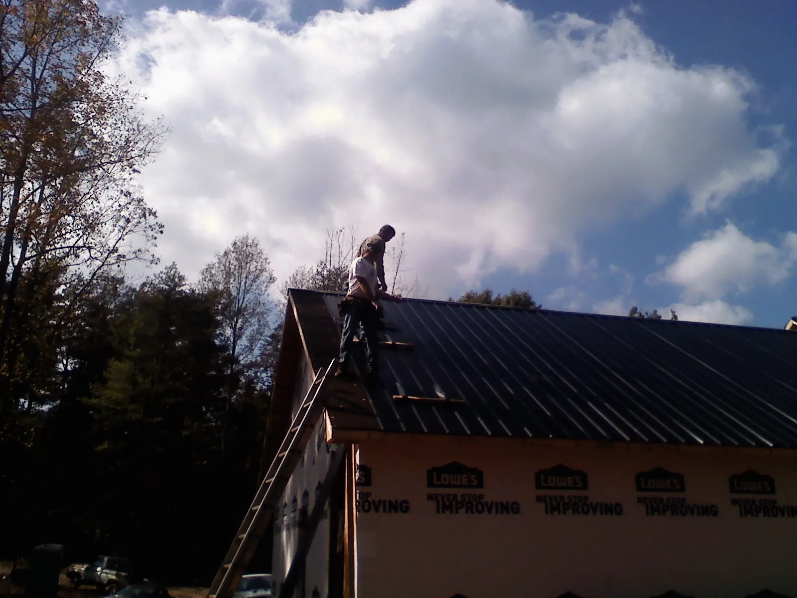 Roofer fastening dark metal panels high against a cloudy sky, from a Roof Inspection job in Talent