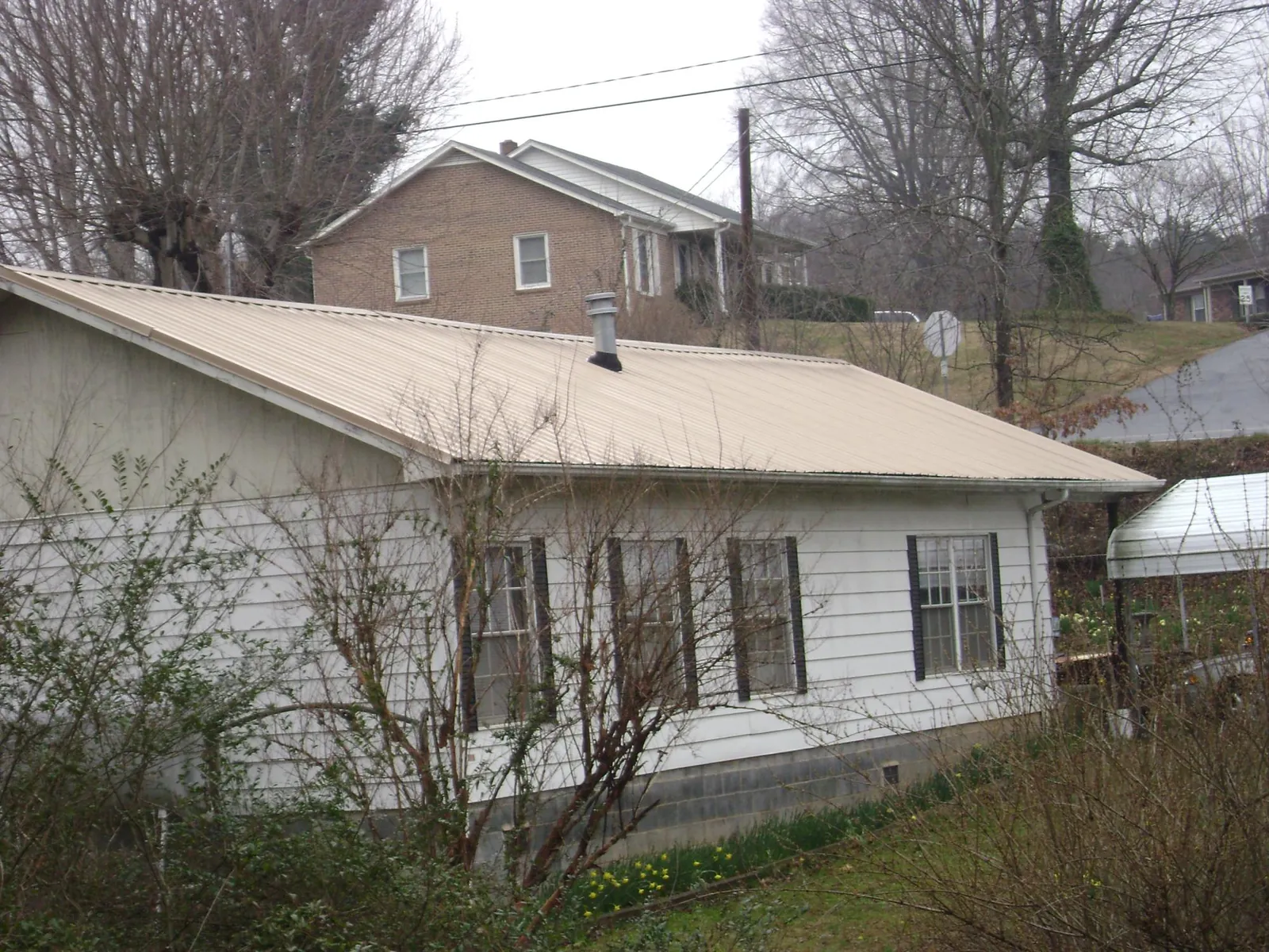 Tan metal roof on a white sided house set into a hillside — Commercial Roofing by Roofing Brothers in Talent